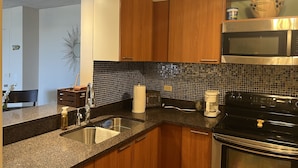 Una cocina con encimeras de granito, gabinetes de madera, un lavamanos de acero inoxidable, un microondas y una estufa.