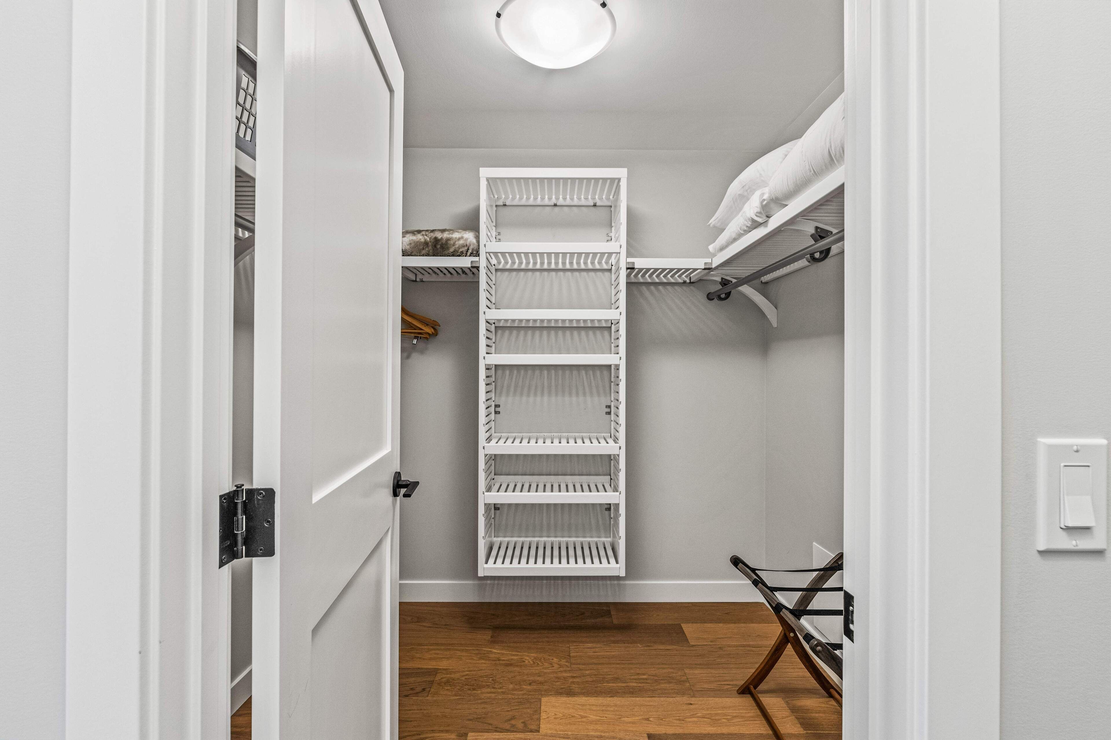 Un vestidor con estantes blancos, una barra para colgar ropa y una pequeña silla de madera.
