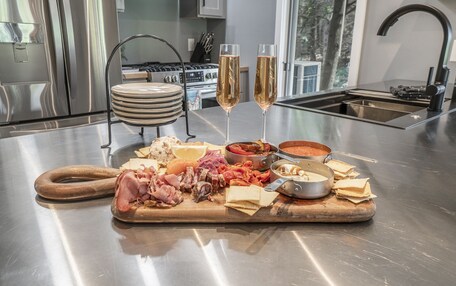 A stainless steel kitchen counter with a charcuterie board, two glasses of champagne, and a stove in the background.