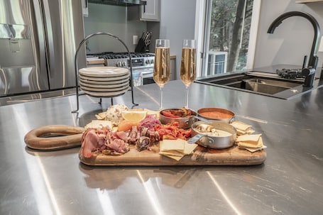 A stainless steel kitchen counter with a charcuterie board, two glasses of champagne, and a stove in the background.