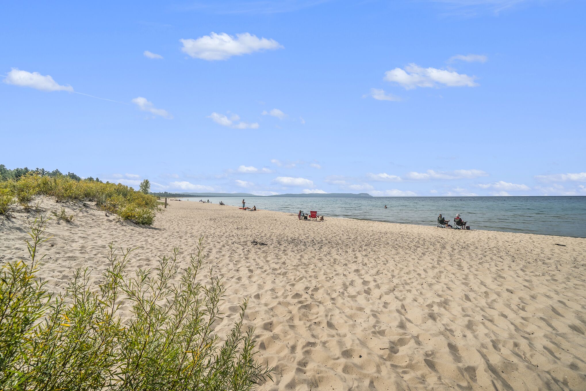 En sandstrand med några få personer och stolar, och en klar himmel.