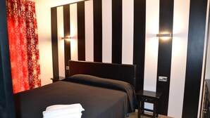 Een hotelkamer met een zwart-wit gestreept hoofdeinde, een bed met een zwart sprei, een nachtkastje en een rood gordijn met patroon.