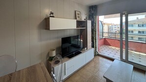 Een moderne woonkamer met een flatscreen televisie, houten paneelwanden, een plafondventilator en een balkon met uitzicht op andere gebouwen.