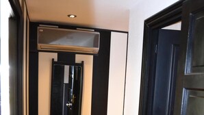 Een hal met een donker houten deur, een spiegel met een zwarte lijst, en een airconditioningsysteem boven een donker houten bureau.
