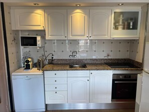 A compact kitchen with white cabinetry, a granite countertop, a built-in microwave, a sink, and a dishwasher.