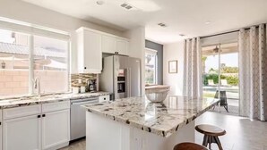 A modern kitchen with white cabinets, a marble island, and a large window. - Beautiful 5 BR house with Olympic size Pool and SPA in Indio (Indio)