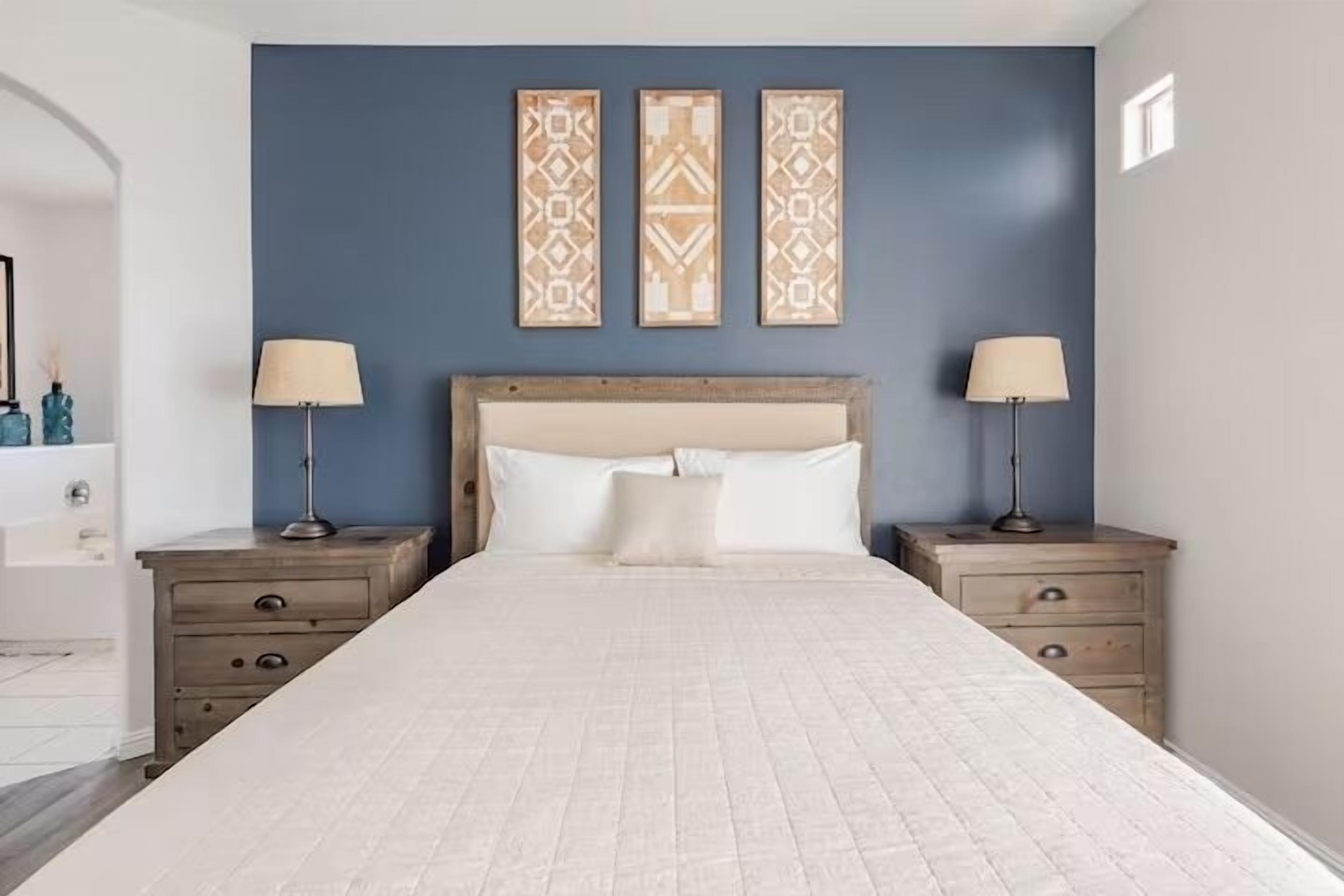 A bedroom with a large bed, two bedside tables with lamps, a headboard, and three wall-mounted decorative panels.