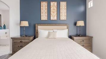 A bedroom with a large bed, two bedside tables with lamps, a headboard, and three wall-mounted decorative panels.