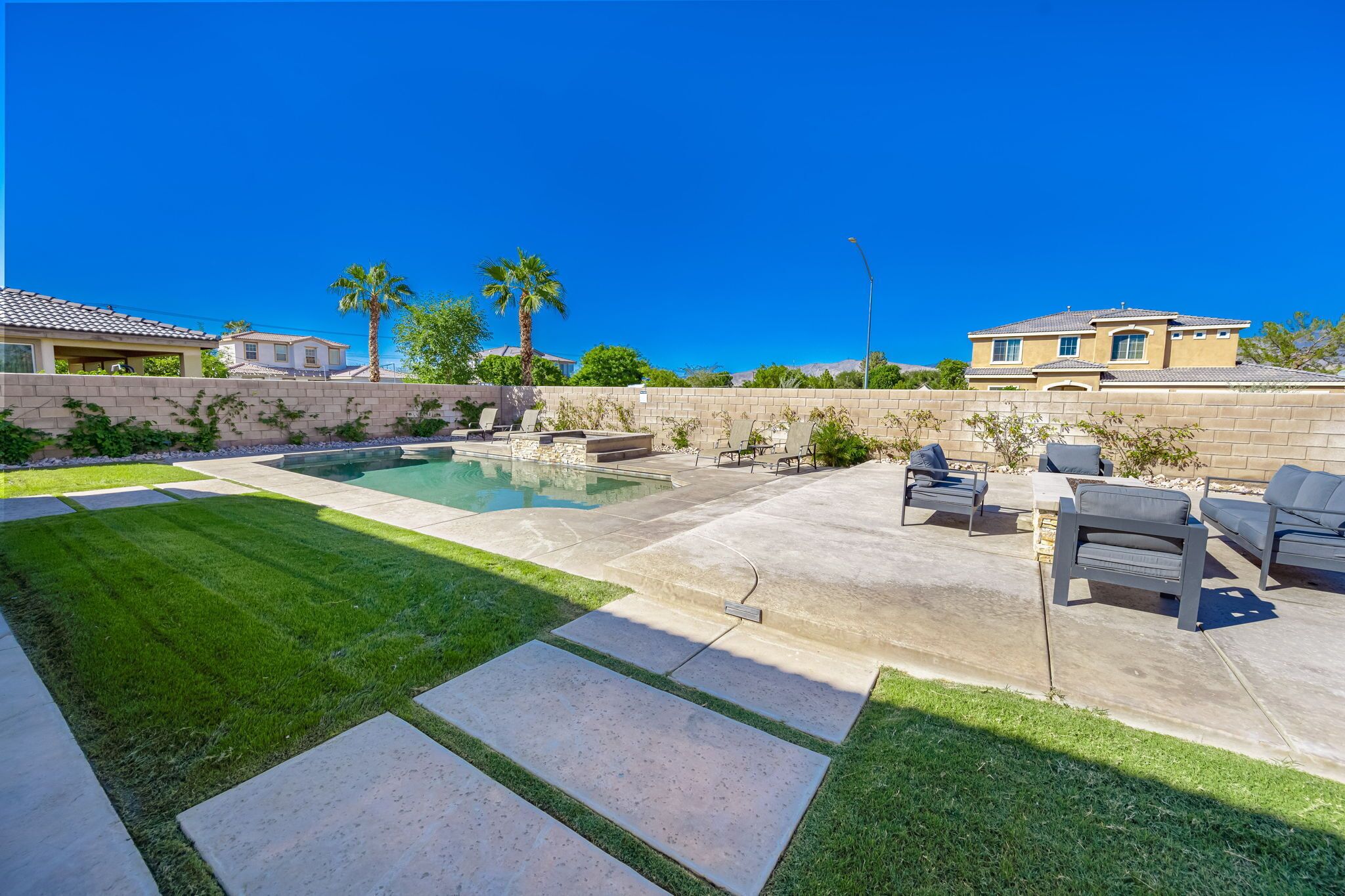 A backyard with a swimming pool, patio furniture, and a well-maintained lawn.