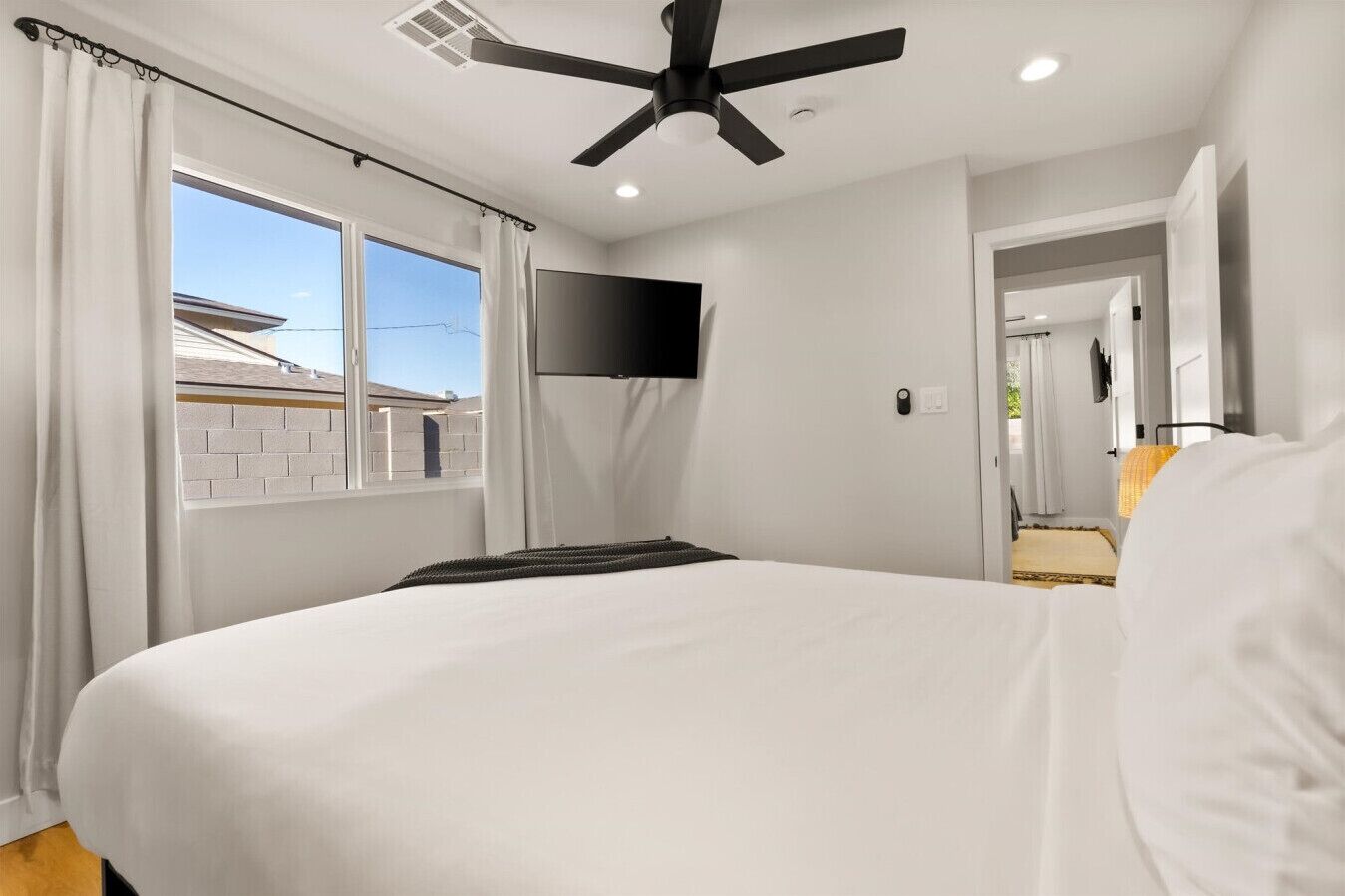 A bedroom with a large bed, a ceiling fan, a flat-screen TV, and a window with curtains.