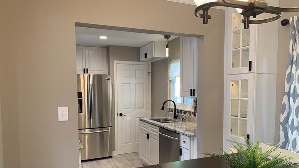 A modern kitchen with a stainless steel refrigerator, white cabinetry, a dark wooden table, and a potted plant. - Spacious, modern 4 bd, 2 bath w/upscale backyard (Columbus)