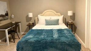 A bedroom with a bed, two bedside tables with lamps, a desk with a chair, and a painting on the wall. - Spacious, modern 4 bd, 2 bath w/upscale backyard (Columbus)