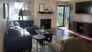 A living room with a fireplace, a sofa, a coffee table, and a television. - Spacious, modern 4 bd, 2 bath w/upscale backyard (Columbus)