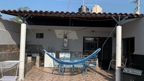 Un espacio de patio cubierto con una hamaca, mobiliario exterior y una parrilla.