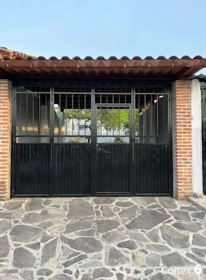 Una reja de metal negro con un acceso empedrado, un muro de ladrillo y un tejado de tejas.