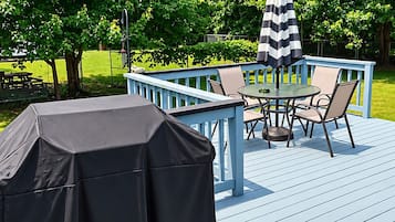 An outdoor deck with a covered grill, a table with chairs, and a striped umbrella.