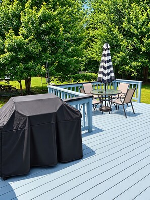 Une terrasse extérieure dotée d’un barbecue couvert, d’une table avec des chaises et d’un parasol à rayures.