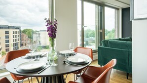 A dining area with a table set for four, large windows, and a green sofa. - The Lux @ Ryedale House -  a premium stay that sleeps 4 guests in 2 bedrooms (York)