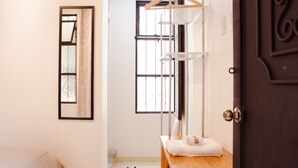 Quarto com cama, cabideiro, um banco e porta.