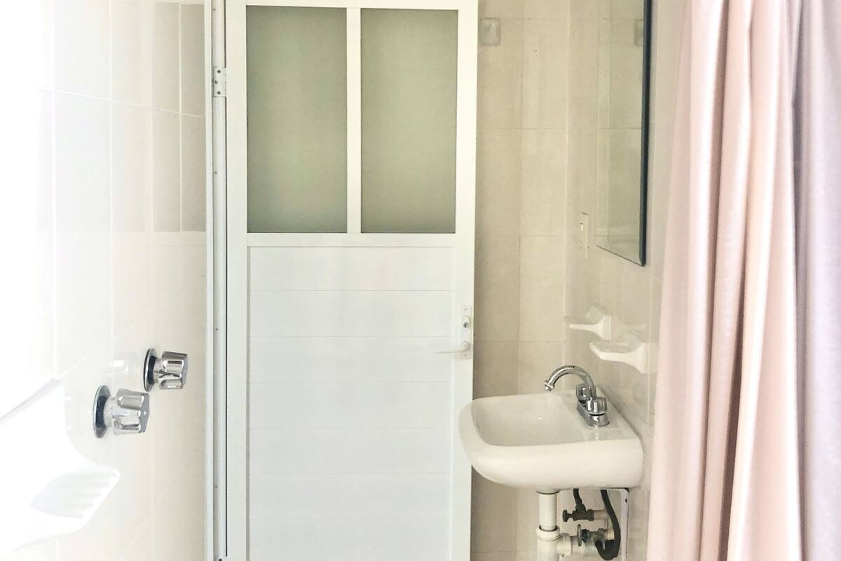 Un baño con ducha, lavamanos y puerta de vidrio satinado.