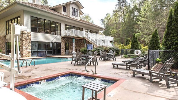 A pool area with lounge chairs and a hot tub, surrounded by a stone building with large windows. - MY LOSS IS YOUR GAIN!  1 bed Villa at MountainLoft (Gatlinburg)