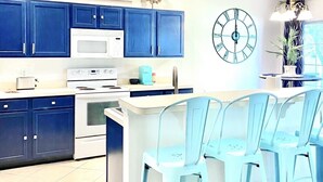 Een moderne keuken met blauwe kastjes, een wit eiland en een grote klok aan de muur.