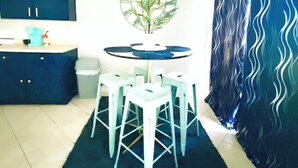 Een eetruimte met een ronde tafel, vier witte stoelen, een blauwe kast en een wandklok.