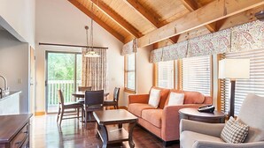 Een ruime woonkamer met een houten plafond, een bank, een salontafel en een eethoek met stoelen en een tafel.