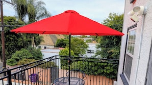 Ein Balkon mit einem roten Sonnenschirm, einem runden Tisch und zwei Stühlen.