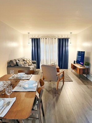 Relax in this inviting living room with a dining table set for a meal, comfortable sofa, and mounted TV.