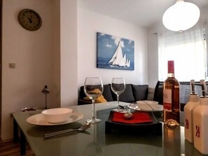 A dining area with a table set for two, a wine glass, a bottle of wine, and a painting of sailboats on the wall.