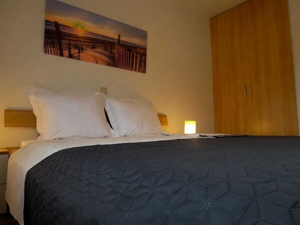 A hotel room with a bed, a nightstand, a wooden wardrobe, and a painting on the wall.