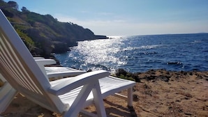Une plage avec des chaises blanches et une côte rocheuse.