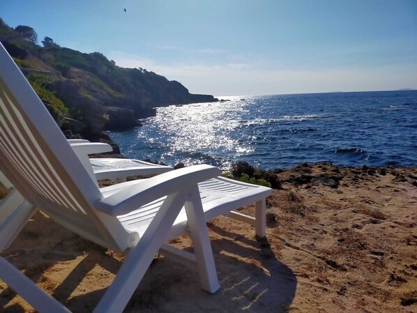 A beach with white chairs and a rocky shoreline.