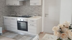 Une cuisine moderne avec des meubles de couleur bois clair, une cuisinière à gaz et un four. On y trouve une table à manger avec des chaises et un vase de fleurs.