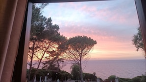 Une vue à travers une fenêtre, avec un coucher de soleil, des arbres et une étendue d’eau.