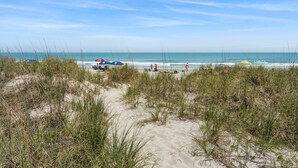 A beach with a clear sky, sandy dunes, and a few umbrellas. - Step into your oceanfront paradise (North Myrtle Beach)