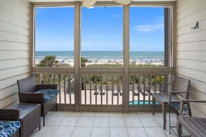 Un balcon avec vue sur la plage, des meubles en osier et une piscine.