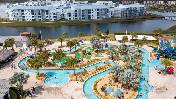Een resort met een groot zwembad, palmbomen en een glijbaan.