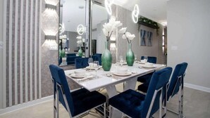 Een moderne eetruimte met een lange tafel, blauwe bekleden stoelen en groene vazen met witte bloemen.