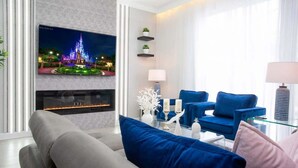Een moderne woonkamer met een flatscreen-tv, een open haard, blauwe en grijze banken en een glazen salontafel.