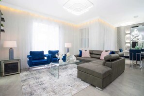 A modern living room with a sectional sofa, a blue armchair, and a glass coffee table.