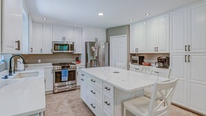 A modern kitchen with white cabinetry, a central island, stainless steel appliances, and a tiled floor. - 15% off 5 nights or more (Ocean Pines)