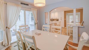 A dining area with a white table and chairs, a hanging light fixture, and a view of the kitchen in the background. - 15% off 5 nights or more (Ocean Pines)