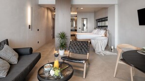 Une chambre d’hôtel moderne, équipée d’un canapé, d’une table à manger avec un plateau, d’un lit et d’une salle de bain visible à travers une porte ouverte.
