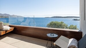 Un balcon avec vue sur la mer, un plancher en bois, une petite table ronde et un fauteuil rembourré.