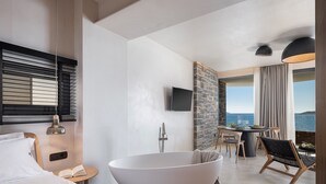 Une chambre d’hôtel moderne dotée d’une grande baignoire, d’un coin repas avec vue et d’un balcon avec table et chaises.