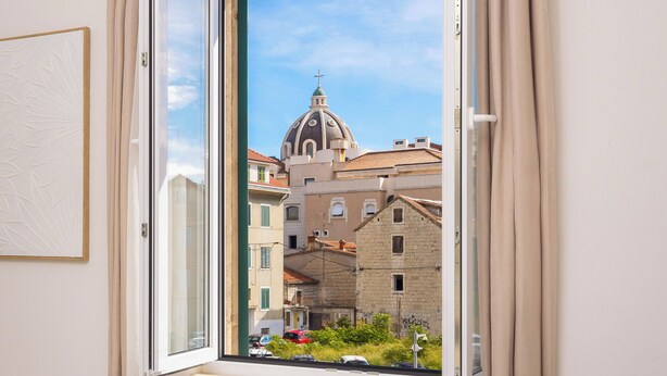 A bedroom with a large window, a bed, and a view of buildings outside.