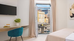 A modern hotel room with a balcony, a flat-screen TV, a desk with a plant, and a bed.