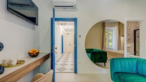 A modern living room with a green sofa, a flat-screen TV mounted on the wall, and a dining area with a wooden table and chairs.